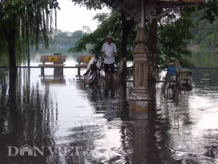 Dưới có hồ, còn phía trên lòng đường, vỉa hè cũng lại thành ao sau mưa Nước không thoát kịp xuống cống, ùn ùn đùn nước lên và chảy tràn xuống hồ Gươm Người đàn ông này bị mắc kẹt trên vỉa hè Nước lênh láng cả một đoạn dài phía đường Đinh Tiên Hoàng Có những chỗ ngập sâu đến nửa mét Bãi để xe ô tô ven hồ Gươm cũng bị ngập khá sâu Nước cống hòa nước mưa, ứ đọng, đen ngòm và kèm theo đó là mùi hôi thối nồng nặc Từng mảng váng bẩn cuộn lại theo dòng nước xoáy tràn xuống hồ Gươm Nước bẩn ào ào xối xuống lòng hồ Dưới có hồ, còn phía trên lòng đường, vỉa hè cũng lại thành ao sau mưa Nước không thoát kịp xuống cống, ùn ùn đùn nước lên và chảy tràn xuống hồ Gươm Người đàn ông này bị mắc kẹt trên vỉa hè Nước lênh láng cả một đoạn dài phía đường Đinh Tiên Hoàng Có những chỗ ngập sâu đến nửa mét Bãi để xe ô tô ven hồ Gươm cũng bị ngập khá sâu Nước cống hòa nước mưa, ứ đọng, đen ngòm và kèm theo đó là mùi hôi thối nồng nặc Từng mảng váng bẩn cuộn lại theo dòng nước xoáy tràn xuống hồ Gươm Nước bẩn ào ào xối xuống lòng hồ