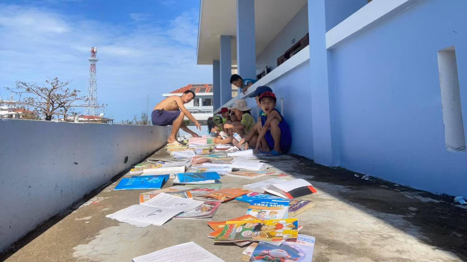 Thầy Nguyễn Hữu Phú - giáo viên Trường Tiểu học xã Song Tử Tây, cùng học sinh phơi khô sách vở đã bị thấm nước. (Ảnh: CTV)