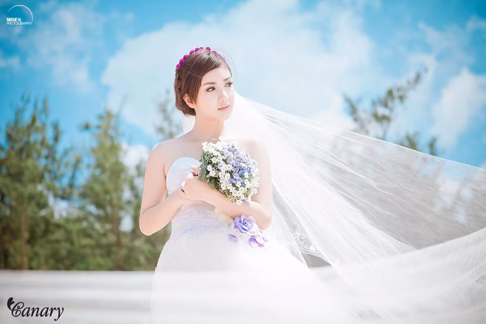 Thiên thần có gương mặt xinh xắn khiến diễn viên Hàn Quốc cũng phải ghen tỵ: Linh Napie tinh khôi trong màu áo cưới. Khăn voan đội đầu kết hợp với vòng hoa tự nhiên tuyệt xinh. Chiếc nơ hoa màu tím ở vòng eo là điểm nhấn nổi bật của chiếc váy cưới.
