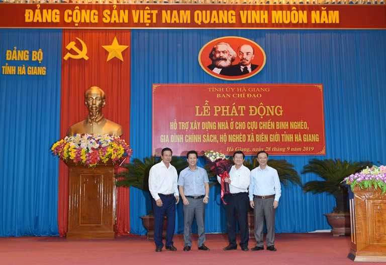 Đại diện Vietcombank, đồng chí Nguyễn Duy Hưng – Phó Trưởng phòng Văn phòng Công đoàn TSC (thứ 2 từ phải sang) trao biển tượng trưng 3 tỷ đồng của Vietcombank tài trợ xây dựng 50 căn nhà cho cựu chiến binh, gia đình chính sách và hộ nghèo tỉnh Hà Giang (Đồng chí Trương Tấn Sang - nguyên Ủy viên Bộ Chính trị, nguyên Chủ tịch nước (thứ 2 từ trái sang) và đồng chí Đặng Quốc Khánh - Ủy viên dự khuyết Ban chấp hành Trung ương Đảng, Bí thư Tỉnh ủy Hà Giang (ngoài cùng bên trái) tặng hoa cho đại diện Vietcombank).