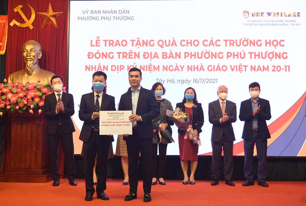 Thầy giáo Đàm Tiến Nam – Hiệu trưởng Trường Nguyễn Bình Khiêm, Cầu Giấy đang trao bộ thiết bị phòng họp trực tuyến cho ông Nguyễn Công Quảng - Phó Bí thư Đảng Uỷ - Chủ tịch UBND phường Phú Thượng. Ảnh: NTCC.