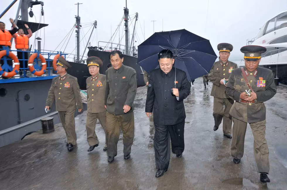Ông Kim Jong-un cầm ô rời khỏi cầu cảng nơi neo đậu của các tàu cá quân sự Bắc Triều Tiên với khuôn mặt vui vẻ Ông Kim Jong-un cầm ô rời khỏi cầu cảng nơi neo đậu của các tàu cá quân sự Bắc Triều Tiên với khuôn mặt vui vẻ