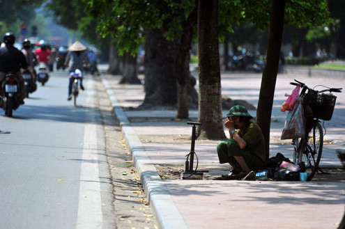 Người bơm xe đạp thu mình dưới tán lá cây lưa thưa để tránh nắng.