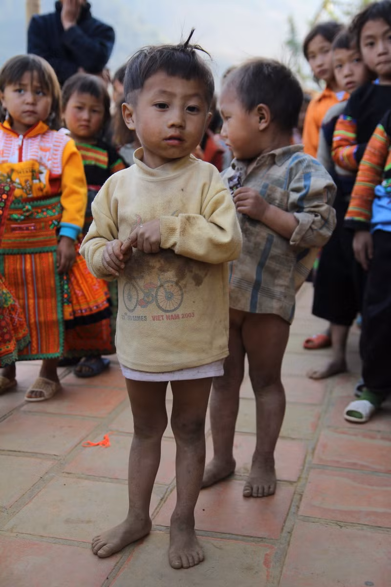 Không có chiếc quần để mặc, dép để đi cậu bé đang tuổi mầm non này phải co chiếc áo mỏng chùm xuống để bớt đi luồng gió lạnh buốt lùa vào chân.