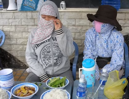 Bà N (trái) luôn bịt kín khẩu trang. Nữ doanh nhân này chỉ mở ra khi ăn cơm, uống nước trước lều bạt căng ngay cổng biệt thự đại gia thủy sản Diệu Hiền. Ảnh: Trúc Linh