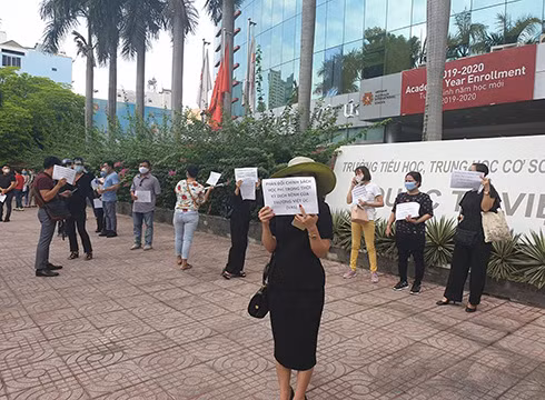 Phụ huynh cầm giấy với dòng chữ in phản đối chính sách thu học phí mùa dịch bệnh của VAS vào sáng 5/5 (ảnh: P.L)