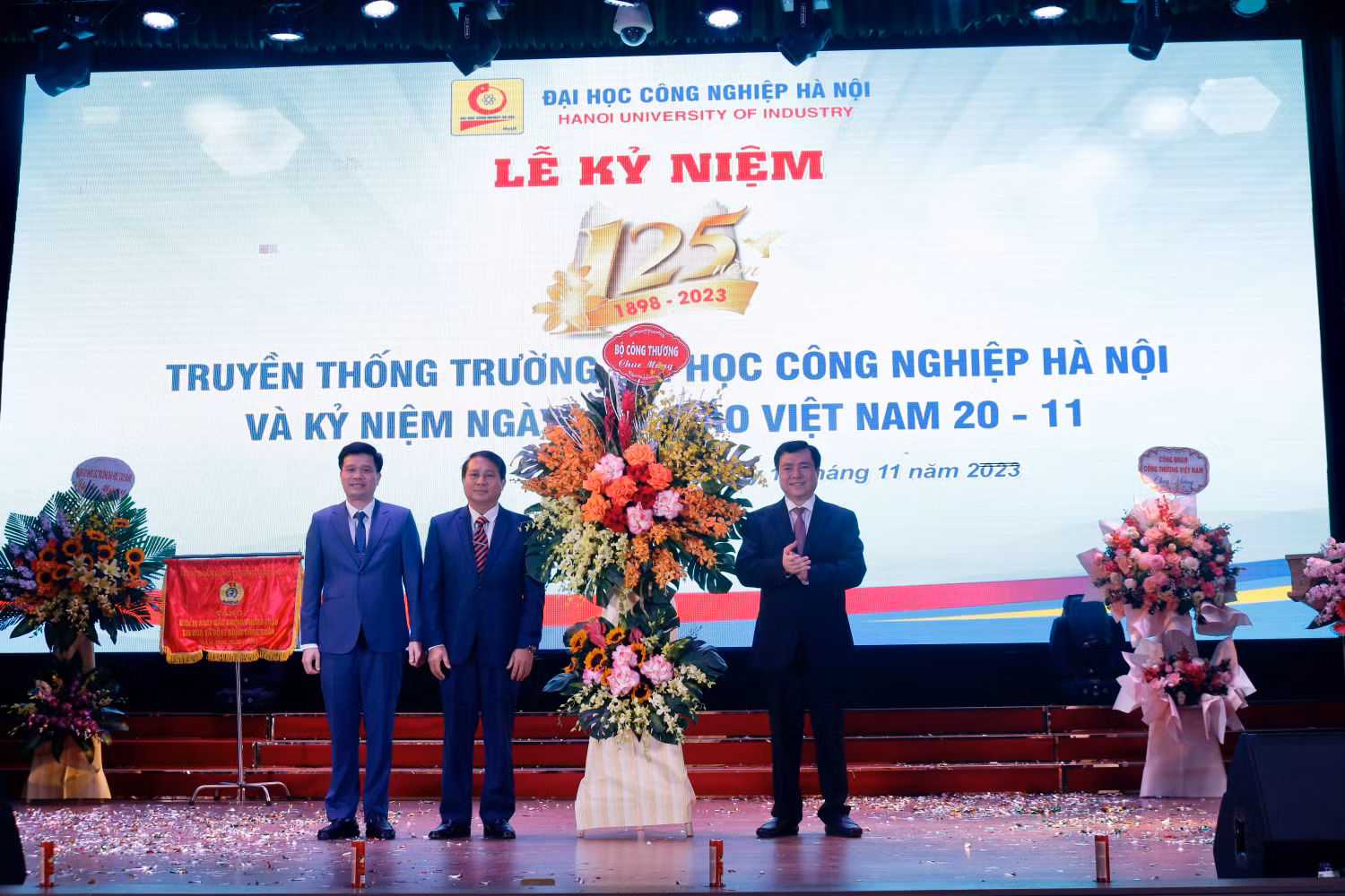 Tiến sĩ Kiều Xuân Thực (ngoài cùng bên trái) cùng Phó giáo sư Lê Hồng Quân (ở giữa) - Chủ tịch Hội đồng trường lên nhận lẵng hoa của Bộ Công Thương chúc mừng nhân dịp 125 năm truyền thống của nhà trường