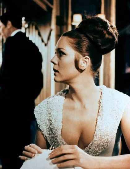 3. Tracy Di Vincenzo (do Diana Rigg đóng), tập phim On Her Majesty’s Secret Service (1969) Kiểu tóc búi to sang trọng này rất dễ thực hiện: - Buộc gập đuôi tóc lên cao giống như tóc đuôi ngựa - Kéo nhẹ đuôi tóc ra xung quanh, tạo thành một búi hình tròn rồi dùng cặp ghim cố định hình dáng. - Cuối cùng, xịt keo giữ nếp 3. Tracy Di Vincenzo (do Diana Rigg đóng), tập phim On Her Majesty’s Secret Service (1969) Kiểu tóc búi to sang trọng này rất dễ thực hiện: - Buộc gập đuôi tóc lên cao giống như tóc đuôi ngựa - Kéo nhẹ đuôi tóc ra xung quanh, tạo thành một búi hình tròn rồi dùng cặp ghim cố định hình dáng. - Cuối cùng, xịt keo giữ nếp