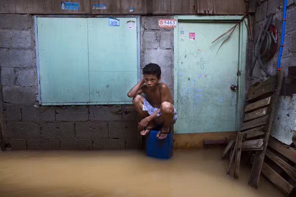 Một người đàn ông đang ngồi trên một chiếc thùng để tránh nước.