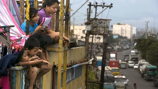Những đứa trẻ đang nhìn xuống thành phố Manila từ một tòa nhà chung cư cao tầng đông đúc trong các khu ổ chuột ở quận Tondo. Do tình trạng quá tải, người dân buộc phải sống thậm chí ở các khu định cư tạm dưới gầm cầu, dọc theo các tuyến đường sắt và thậm chí cả trong nghĩa trang.