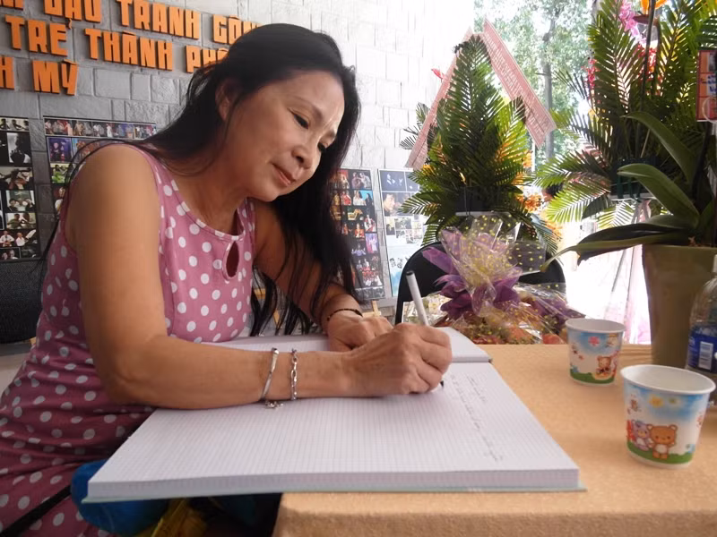 NSƯT Kim Xuân đang viết cảm nghĩ về buổi triển lãm. Chị là 1 trong 300 nhân vật tiêu biểu của ống kính Nguyễn Á.