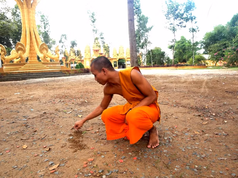 Vị sư trẻ người Khơme này đang viết trên nền đất bằng tiếng Việt tên ngôi chùa cho phóng viên xem.