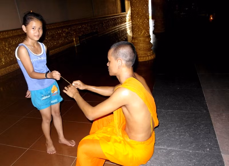 Vị sư trẻ đang buộc dây chỉ cầu may mắn cho một cô bé.