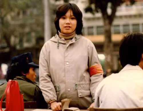 Thiếu nữ "băng đỏ" xinh đẹp với một trong những cách mặc thời trang nhất giữa thập niên 80: Áo len cổ lọ bên trong, áo lông Đức bên ngoài. Người ngồi bên cạnh cũng rất hợp thời cùng áo Nato và mũ bò kiểu Levi's