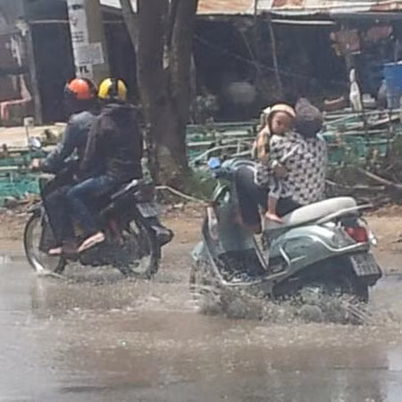 Vừa bế con vừa phóng xe qua đoạn đường ngập.