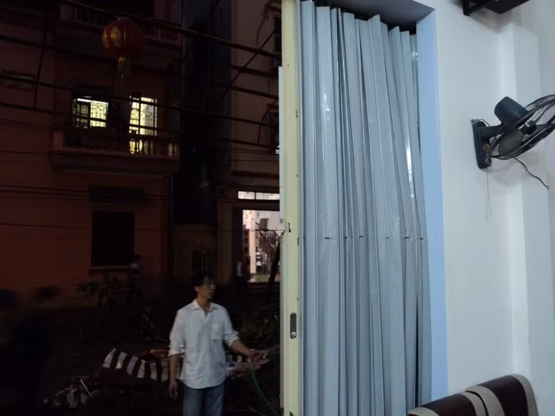 Một người dân đang rửa tường nhà mình và cả tấm cửa thép bị biến dạng do ảnh hưởng bởi vụ nổ kinh hoàng