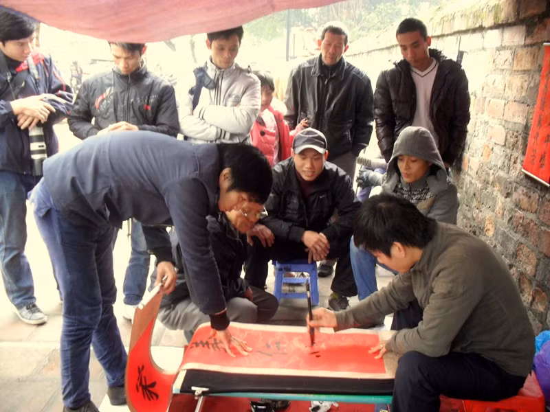 "Ông đồ" trẻ này đang viết một vế câu đối đỏ, nhiều bạn trẻ khác đứng xem.