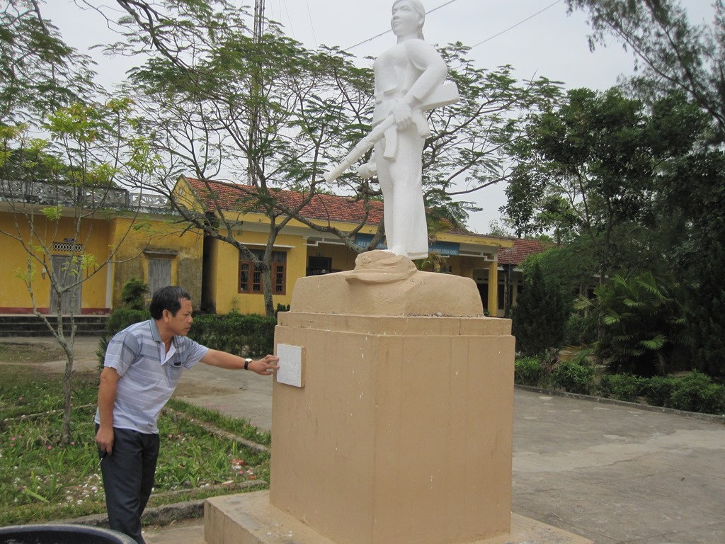 Cựu chiến binh Hoàng Như Lý bên tượng đài liệt sĩ Hoàng Thị Hồng Chiêm đặt tại trường Trung học cơ sở Bình Ngọc (Ảnh: Lại Cường)
