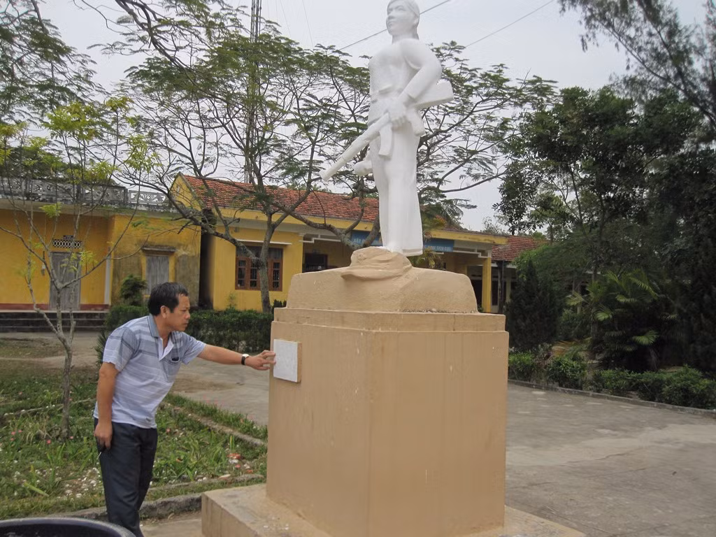 Cựu chiến binh Hoàng Như Lý bên tượng đài liệt sĩ Hoàng Thị Hồng Chiêm đặt tại trường Trung học cơ sở Bình Ngọc (Ảnh: Lại Cường)