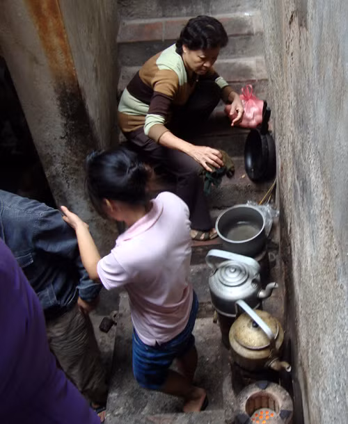 Một phụ nữ luộc trứng và một cô gái đang nấu nước bằng bếp than tổ ong ngay khoảng không gian dẫn lên cầu thang trên gác hai (ảnh chụp tại ngõ 44 Hàng Buồm) - Ảnh: My Lăng.