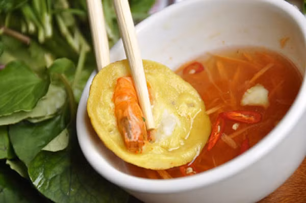 Muốn có bánh ngon phải ngâm gạo trước, sau đó xả lại nhiều nước cho hạt gạo trắng, trộn vào chừng một chén cơm (để nguội) và một ít dừa nạo (để nguyên xác) xay chung tất cả bằng cối đá. Khi có được thau bột mịn, lỏng vừa thì nêm nếm gia vị, để hành xắt mịn, tiêu… khuấy đều. Nhờ trộn cơm và dừa xác nên cái bánh “ra lò” vừa xốp vừa dai, lại béo rất thơm ngon. Có thể ăn bánh với rau sống, dưa leo hoặc chỉ ăn với nước mắm chua cay thôi cũng được, nhưng phải ăn nóng.