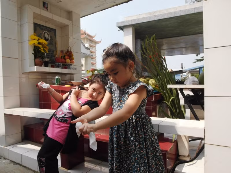 Bí Ngô tạo dáng bên mộ người bạn thân của bố, trong khi Hạt Dẻ nghịch với chiếc khăn giấy.