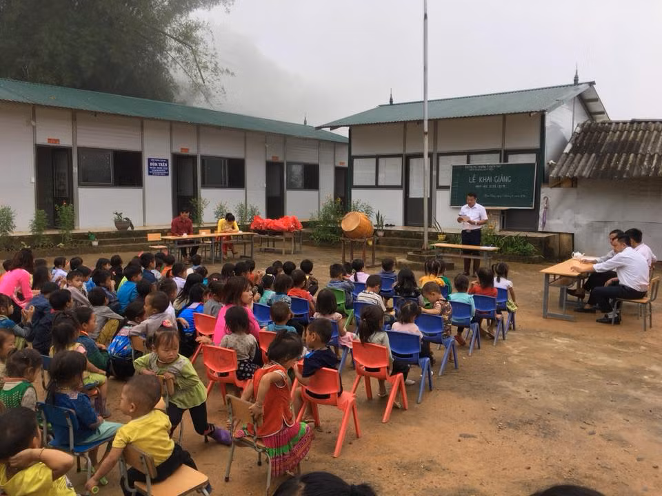 Lễ khai giảng được tổ chức ở điểm trường, có không ít học sinh phải địu theo đi khai giảng. Em ngồi ghế, còn chị ngồi đất.