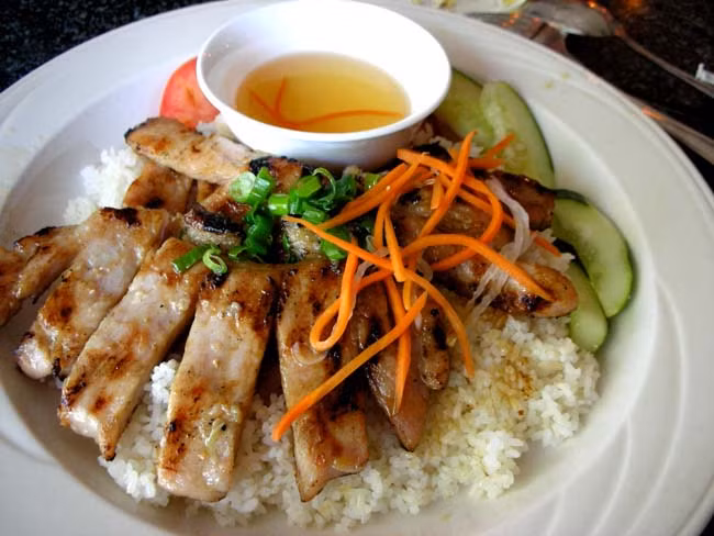 25. Cơm sườn nướng: Thịt sườn cốt lết có cả phần xương hay nạc thăn lưng, xắt miếng lớn dày bằng bàn tay đem nướng trên lửa lớn cho chín đều. Trong lúc nướng, tưới thêm nước gia vị lên thịt cho miếng thịt chín không bị khô. Sườn nướng ăn với cơm trắng bình thường hoặc cơm tấm, chan nước mắm chua ngọt, ăn kèm với dưa chuột, cà chua, cải chua rất ngon. Ăn đâu: Cơm tấm Thuận Kiều, quận 5, TP.HCM.