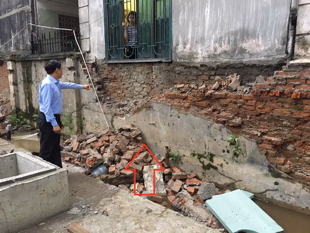 Bồn chứa dầu ngầm của dự án FLC Twin Towers nằm sát ngay cạnh nhà dân (mũi tên đỏ). Trong ảnh người dân đang chỉ vào bức tường cũ bị đơn vị thi công dự án tự ý đập phá, xâm phạm đến móng nhà nhiều hộ dân liền kề. Ảnh: V.P.