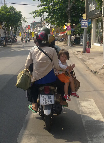 Xe máy hết chỗ ngồi, em bé phải ngồi trên đùi mẹ, quay ngược lại. Ảnh: Nguyễn Văn Tình. Xe máy hết chỗ ngồi, em bé phải ngồi trên đùi mẹ, quay ngược lại. Ảnh: Nguyễn Văn Tình.