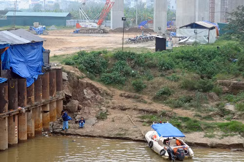 Dưới bờ sông, hai người đàn ông mặc đồng phục đang ngồi câu cá. Theo lời nhân viên bảo vệ, họ là những công nhân thi công tại đây.