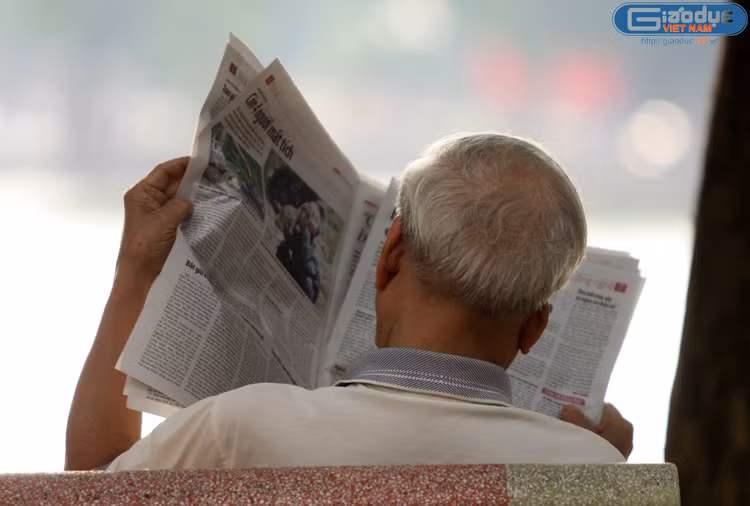 Một ông cụ ngồi đọc báo mới ra.