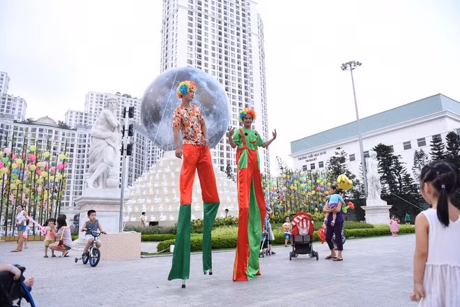 Quảng trường Vincom Mega Mall Royal City trở thành một sân chơi sôi động đậm chất lễ hội. Từ 17 giờ chiều, trong lúc chờ thắp sáng “siêu trăng”, rất đông người đã tề tựu tham gia hoạt động thú vị như treo điều ước lên hàng tre ước nguyện, chụp ảnh lấy ngay miễn phí, xem biểu diễn đi cà kheo...