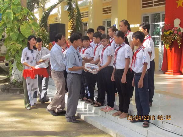 Thầy Phan Văn Hùng, Hiệu trưởng Trường Trung học cơ sở Mỹ Hưng (thứ hai) phát bảo hiểm y tế cho học sinh nghèo cùng với lãnh đạo huyện nhân ngày khai giảng năm học mới, 5/9/2016. (Ảnh tác giả cung cấp)