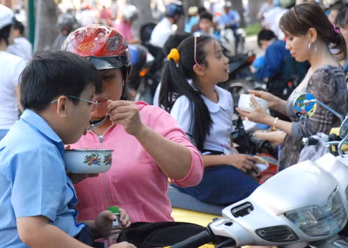 Cha mẹ tranh thủ cho con ăn ngoài đường cho kịp giờ học thêm ở TP.Hồ Chí Minh, ảnh trên báo Người Lao Động của tác giả Tấn Thạnh