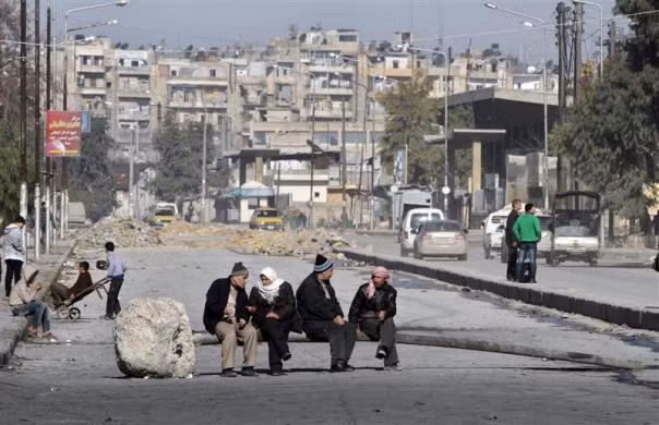 Những người đàn ông ngồi trên chiếc cột điện đổ ngang đường phố ở Aleppo, Syria ngày 16/12.