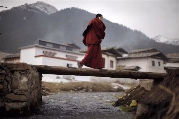 Một tu sĩ nói chuyện qua điện thoại khi đi ngang qua cây cầu gần một ngôi chùa ở Langmusixiang ngày 22/2.