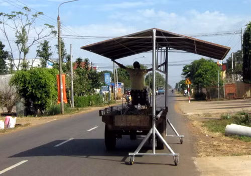 "Dân chơi chế tạo chiếc xe không sợ mưa rơi". Người thanh niên dùng hai chân điều khiển xe, còn hai tay thì lo giữ cái mái hiên di động có gắn bốn bánh xe lưu thông trên đường trông thật là đáng sợ. Chụp tại huyện Châu Đức, tỉnh Bà Rịa - Vũng Tàu. Ảnh: Sơn Khê.