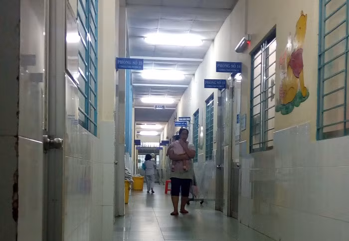 Bên ngoài hành lang của phòng bệnh, ông bố và bà mẹ trẻ vật vã dỗ dành con trẻ.